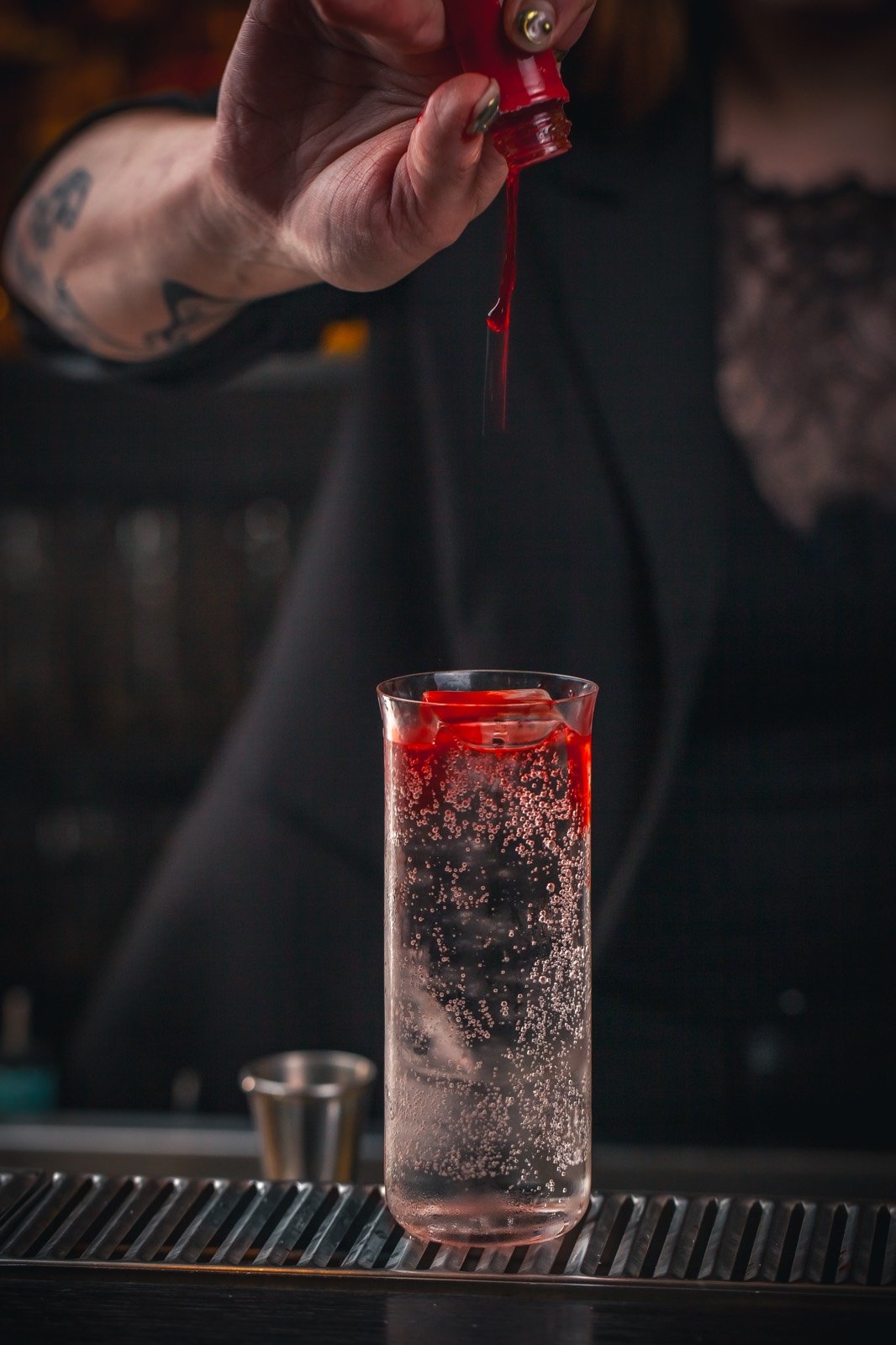 Le geste précis d’un bartender versant un ingrédient rouge dans un cocktail pétillant